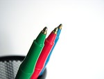 Free Stock Photo: Closeup of three colored pen tips in a black wire pen holder on a white background.