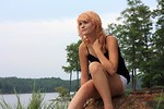 Free Stock Photo: A beautiful young woman posing on a rock by a lake