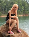 Free Stock Photo: A beautiful young woman posing on a rock by a lake