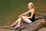 Free Stock Photo: A beautiful young woman posing on a rock by a lake