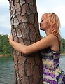 Free Stock Photo: A beautiful young woman hugging and kissing a tree by a lake