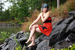 Free Stock Photo: A beautiful young woman posing in a red dress on rocks by a lake.