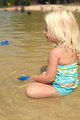 Free Stock Photo: While she and her family were at a lake on a sunny Georgian day, the young girl pictured was seated near the lake\'s shoreline wearing her bright turquoise-yellow colored swimsuit. It appears that she was playing with a blue floating toy she\'d brought with her from home.