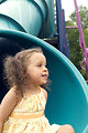 Free Stock Photo: Dressed in a bright yellow sleeveless dress, this smiling young girl was having fun playing on the rides at a community park. In this view, she was seated on a slide, having completed her downhill ride.