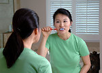 Free Stock Photo: An Asian woman brushing her teeth in a mirror