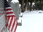 Free Stock Photo: Closeup of a US flag and tombstone in a snow covered graveyard.
