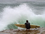 Free Stock Photo: A man with a surf board watching waves crash on a rock