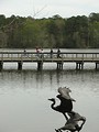 Free Stock Photo: People riding bikes across a bridge with a bird statue in the foreground