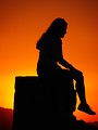 Free Stock Photo: Silhouette of a young girl sitting on a rock before a sunset.