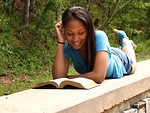 Free Stock Photo: A beautiful African American teen girl reading a book on a stone wall in the woods