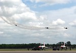 Free Stock Photo: Four AH-1F Cobra attack helicopters flying over Thunderbird jets on a runway with smoke trails in the sky