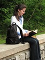 Free Stock Photo: A young schoolgirl reading a book on a stone wall outside